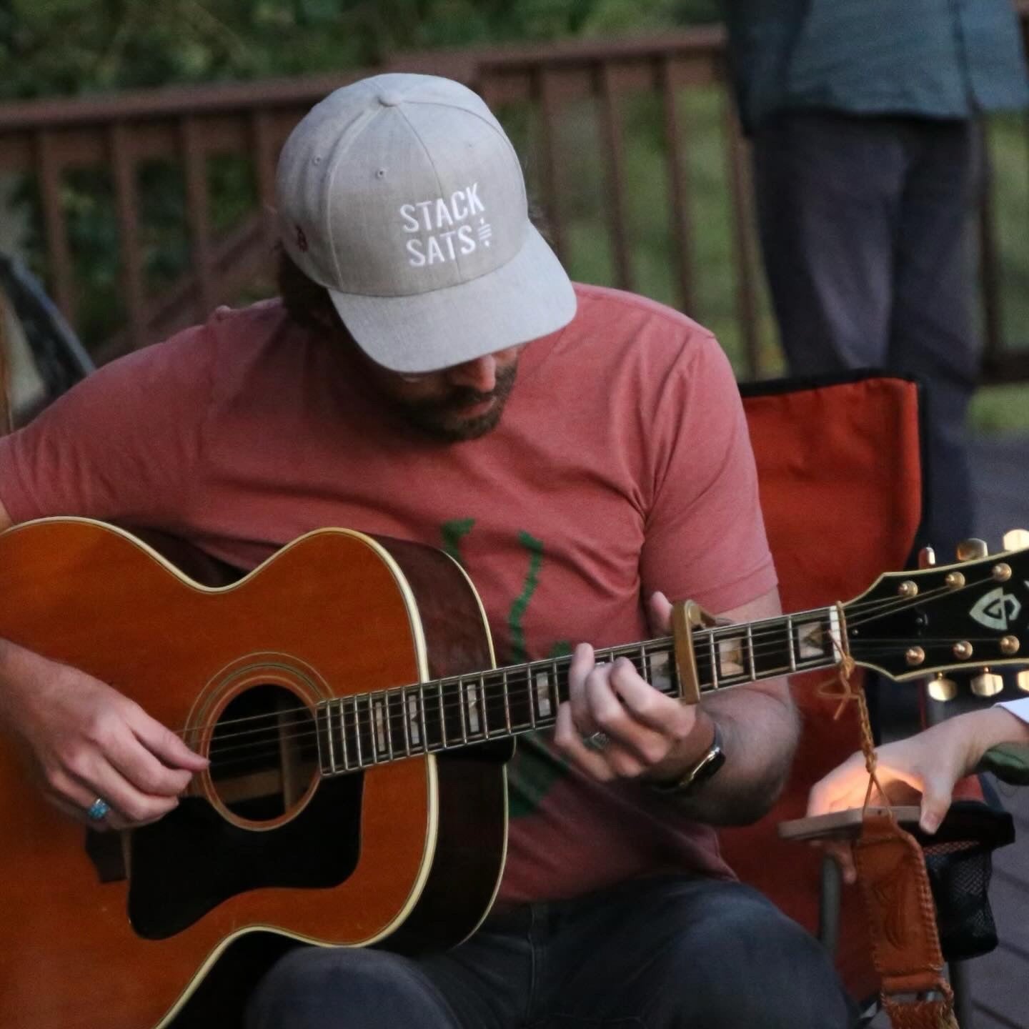 A model wears a heather grey hat with the words 'STACK SATS' embroidered on the front in white. He's holding a guitar and wears a turquoise ring.