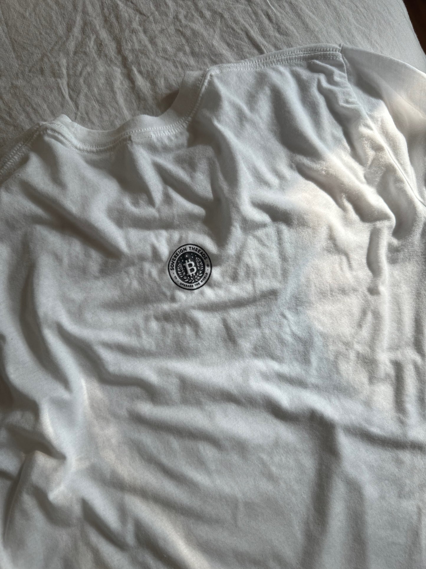 A white t-shirt with a black Sovereign Goods logo on the back.