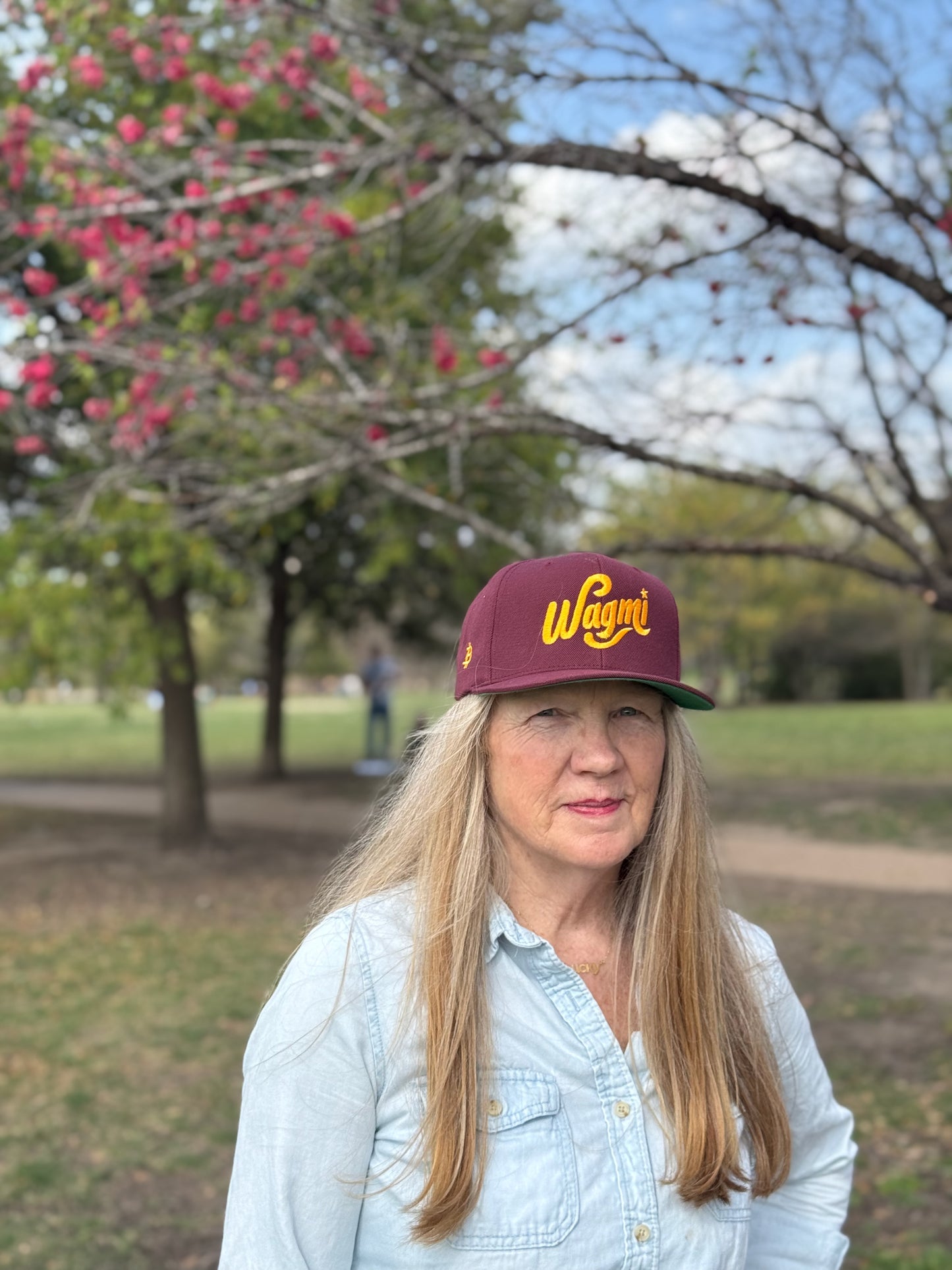 A female model wearing a maroon baseball cap that reads WAGMI (We’re All Gonna Make It) embroidered in yellow.