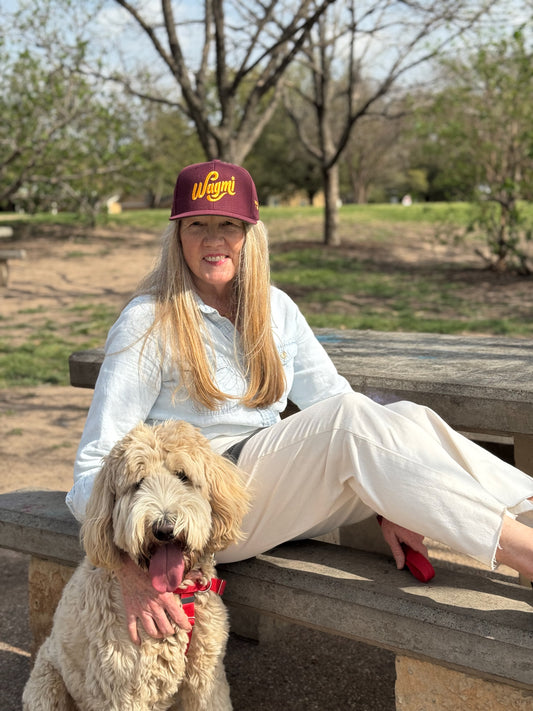A female model sits with her dog wearing a maroon baseball cap that reads WAGMI (We’re All Gonna Make It) embroidered in yellow.