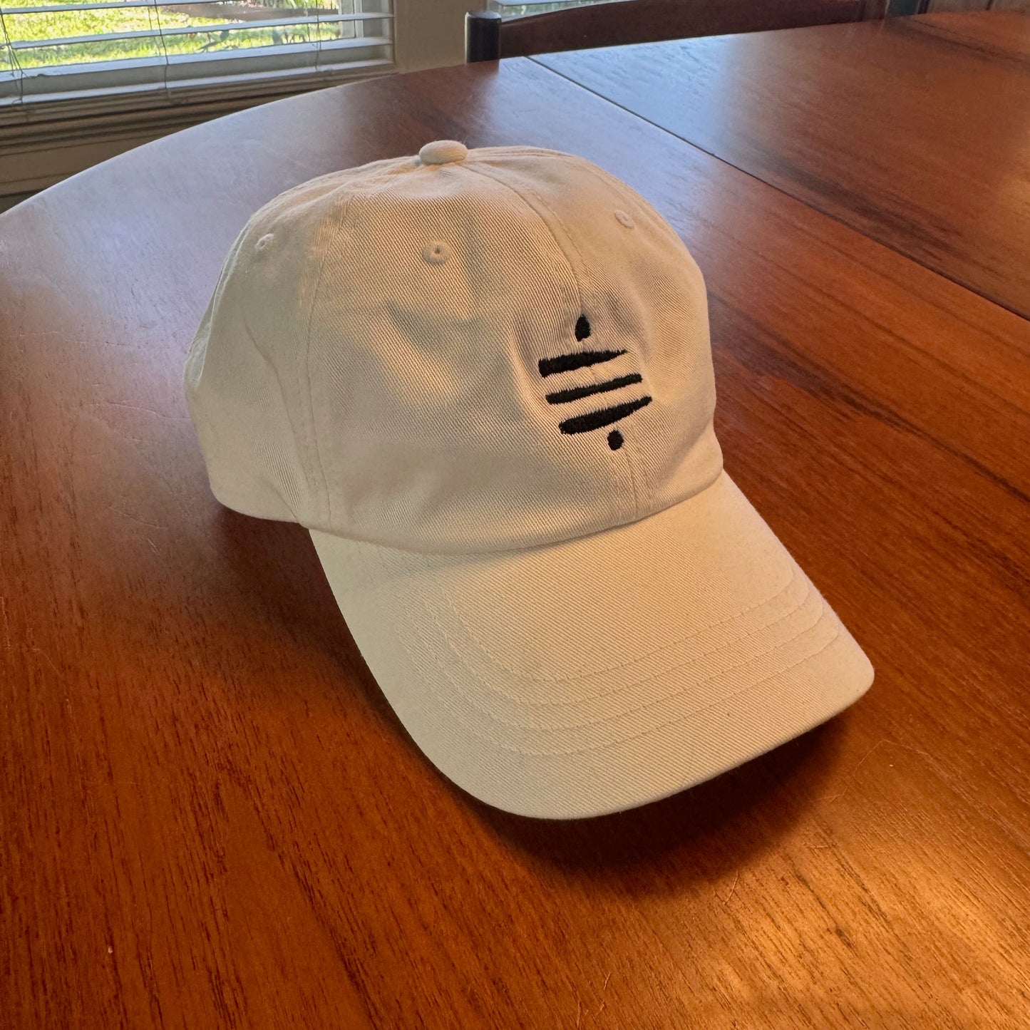 White dad hat with black Satoshi symbol embroidery, honoring Bitcoin’s creator - Sovereign Goods.