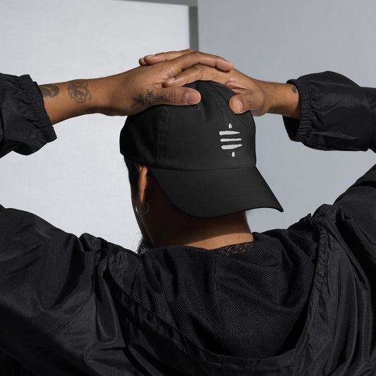 A model with tattoos wears a black dad hat backwards with the Satoshi Symbol embroidered in white on the front.
