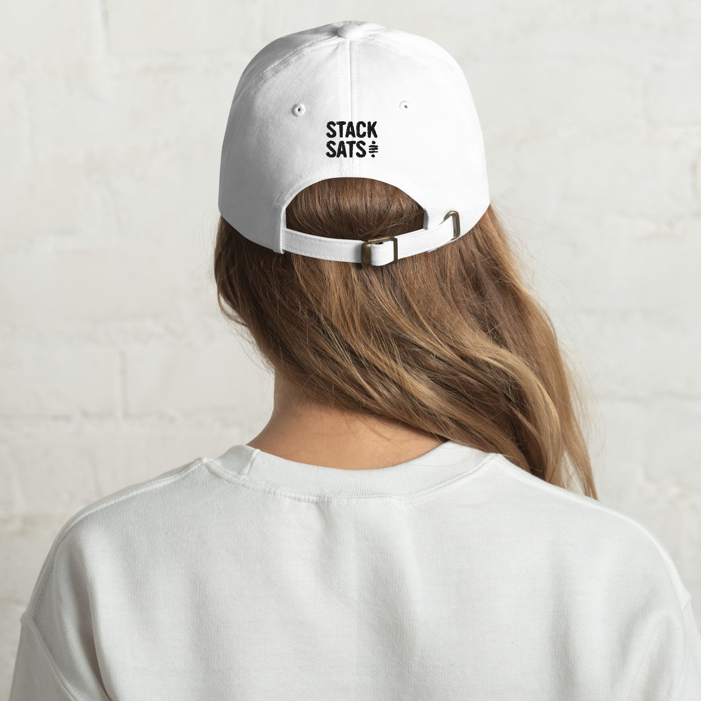 A female model wears a white dad hat with 'STACK SATS' embroidered in black on the back.