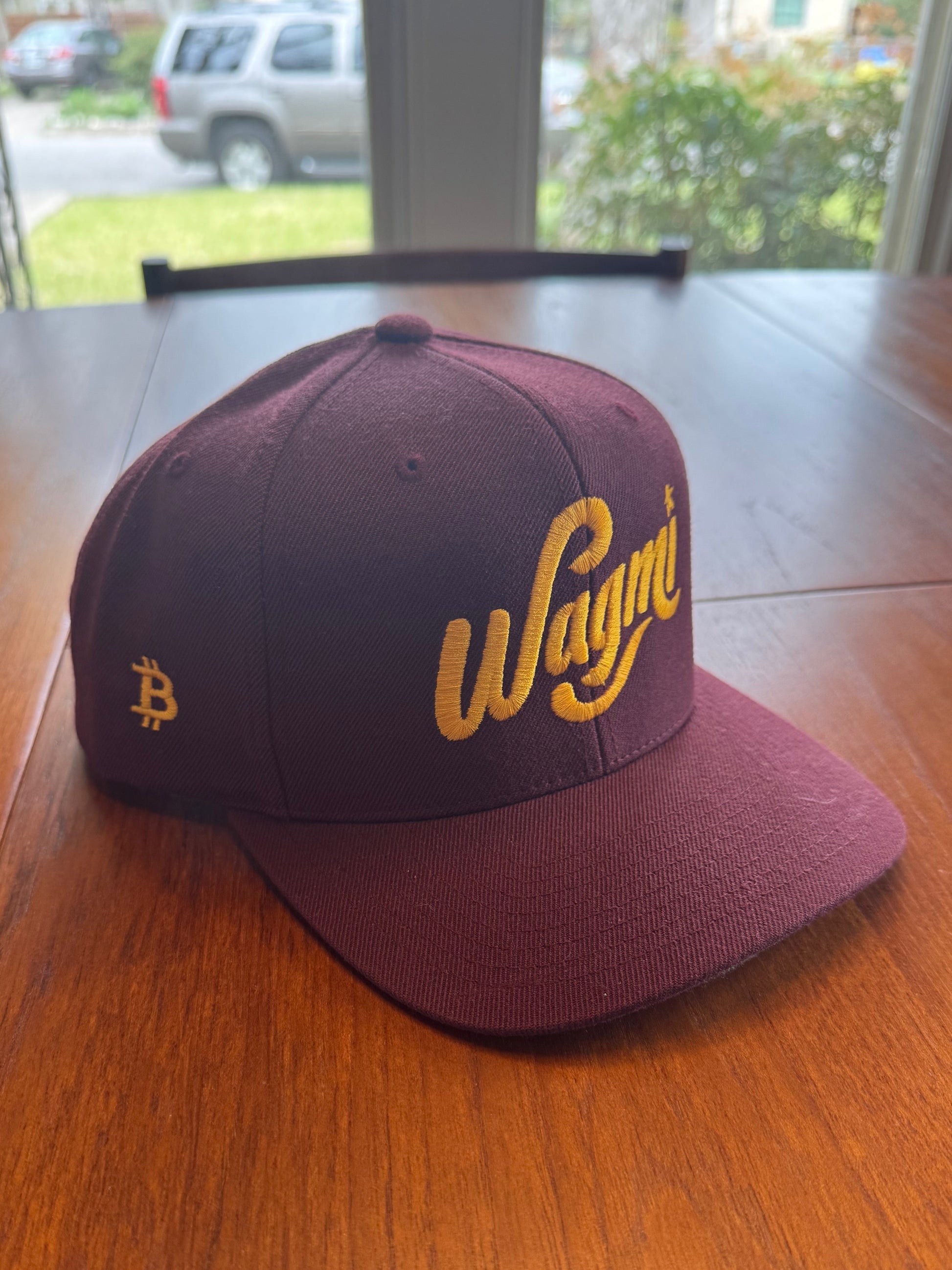 Maroon snapback hat with yellow bitcoin logo and WAGMI 'We’re All Gonna Make It' text for crypto optimism - Sovereign Goods.