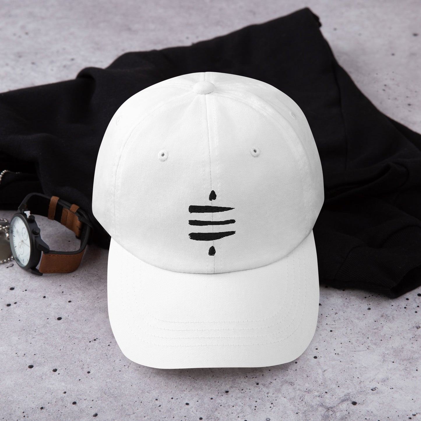 A white dad hat with 'STACK SATS' embroidered in black on the back lays next to a watch with a leather band and a black garment.